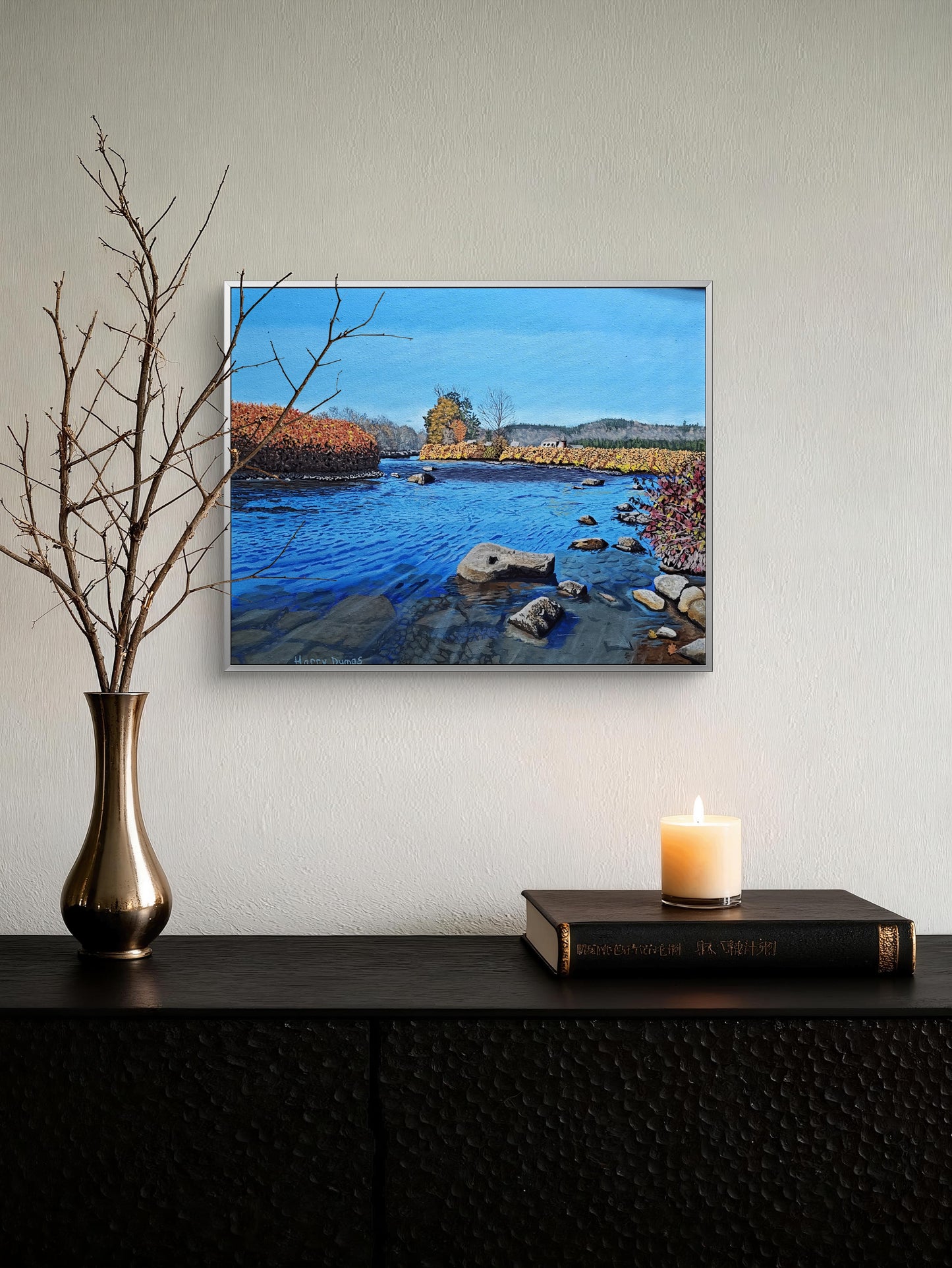 Deerfield River oil painting, oil on a 20 x 26 inch canvas. Framed artwork of a landscape with a river and trees on a wall above a dark surface with a candle and vase.